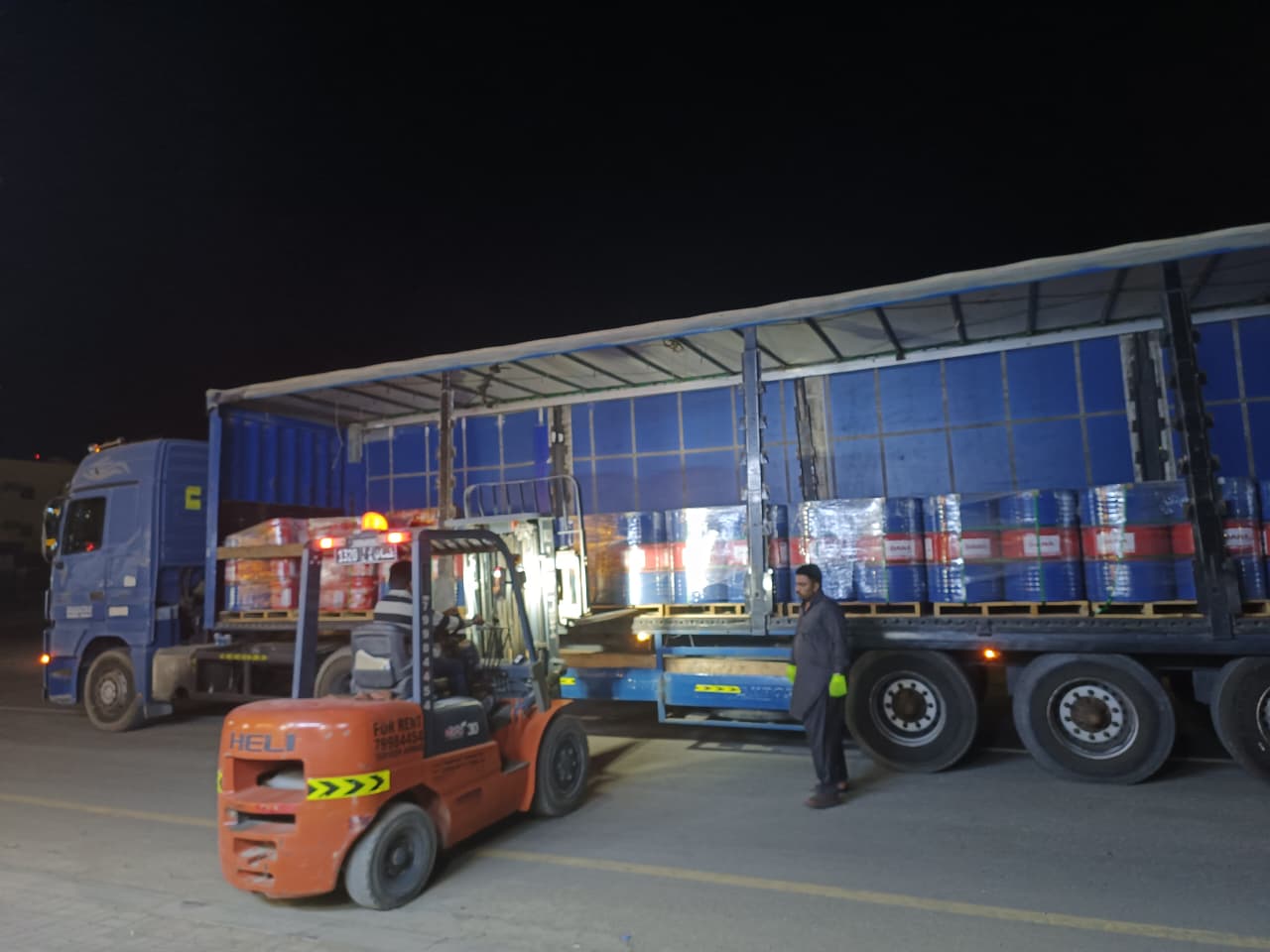 Forklift loading cargo onto blue industrial truck at night in warehouse facility